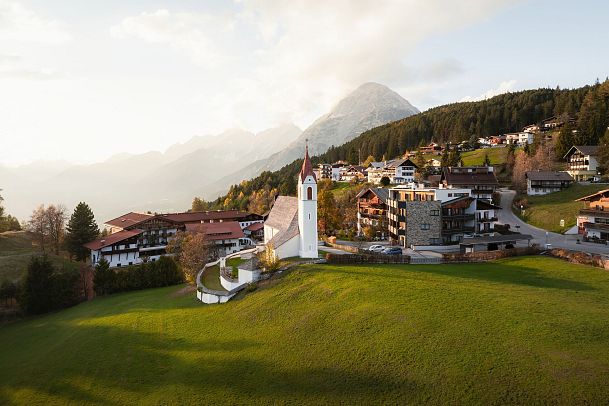 drohnenaufnahme-moesern-im-herbst-kirche-mit-hohe-munde-bei-sonnenuntergangsstimmung-1