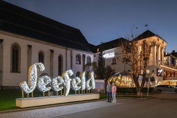 lichterpark-seefeld-2024-mann-und-frau-stehen-vor-seefeld-logo-im-dorfzentrum-1