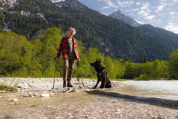 spaziergang-mit-hund-in-unterleutasch-mann-steht-mit-hund-am-fluss-8