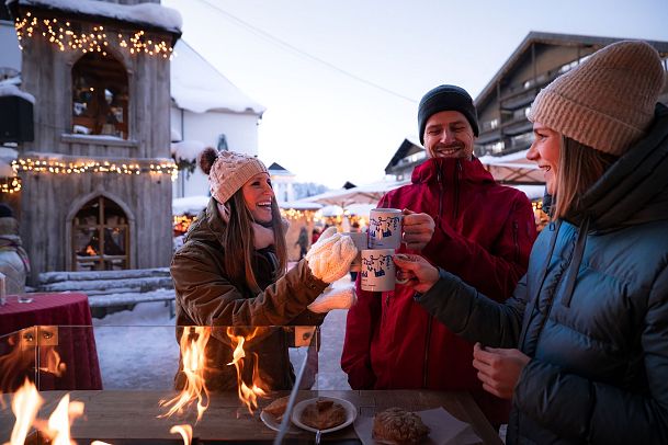 weihnachtsmarkt-mit-menschen-drei-freunde-stossen-mit-gluhwein-an-glockenturm-links-feuer-zu-sehen-15