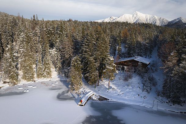 winterwandern-paar-moeserer-see-drohnenaufnahme-paar-steht-am-steg-mit-moeserer-seestube-und-reither-spitze-im-hintergrund-1-1