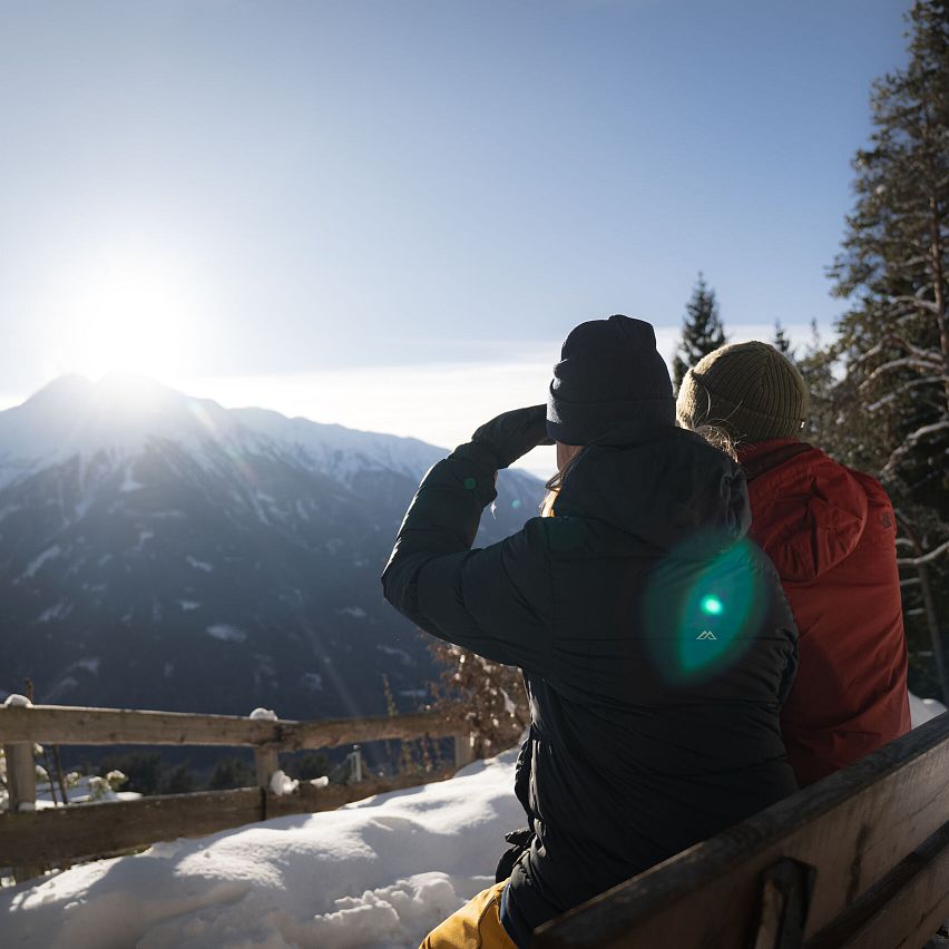 Winterwandern Paar Möserer See Paar sitzt auf Bank und blickt in Inntal Frau hebt Hand