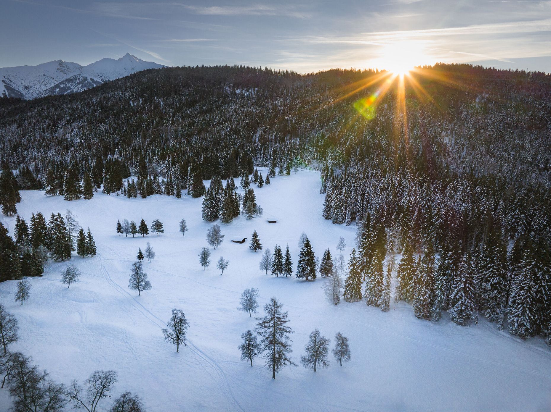 Wildmoos im Winter Drohnenaufnahme Blick Richtung Reither Spitze mit Sonnenstern Bäumen und 2 kleinen Hütten (1)