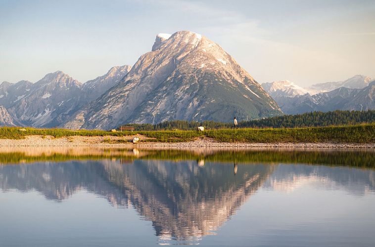 drohnenaufnahme-gschwandkopf-speichersee-person-laeuft-entlang-des-speichersees-mit-hohe-munde-im-hintergrund