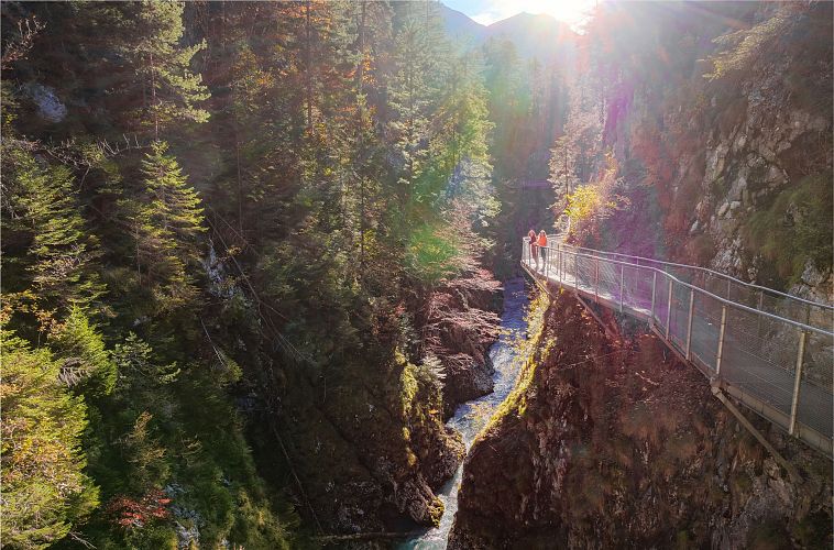 geisterklamm-im-herbst-drohnenaufnahme-zwei-frauen-auf-dem-steg-mit-flusslauf