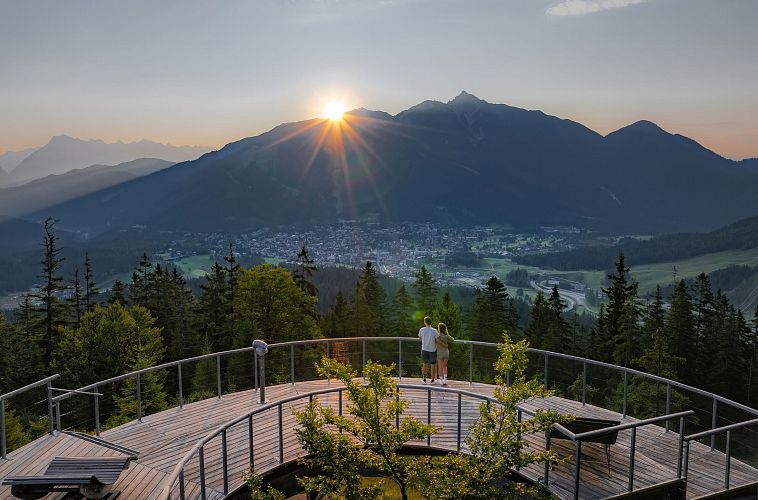 sonnenaufgang-aussichtsplattform-bruschkopf-drohnenaufnahme-paar-steht-am-gelaender-der-plattform-sonnenstern-ueber-seefelder-spitze-2