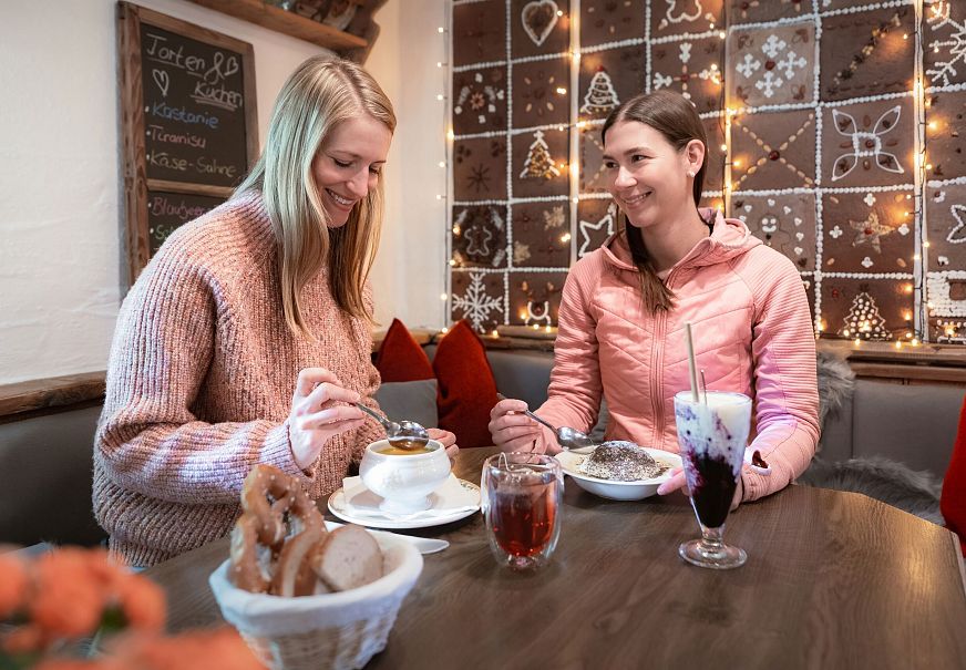 sub1-polis-huette-im-winter-zwei-frauen-kehren-ein-in-der-huette-frau-laechelt-andere-frau-an